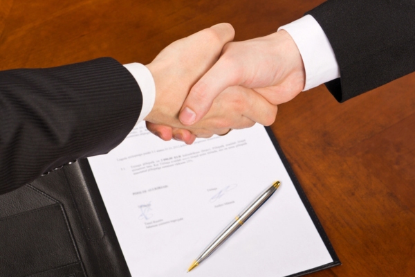 cropped view of two men shaking hands with a signed contract in the background