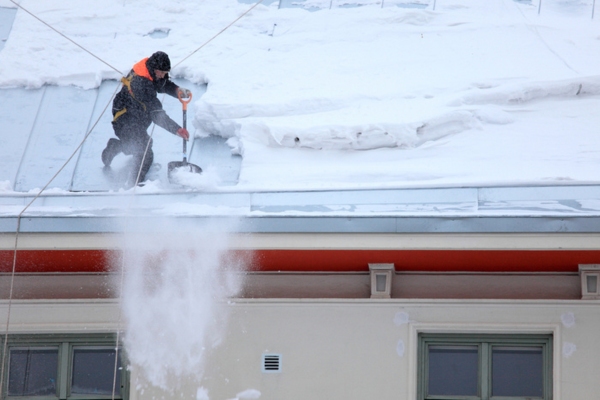 man de-icing a snowy roof depicting harsh winter condition