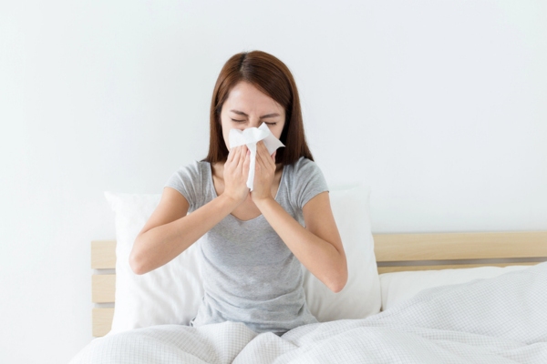 woman sneezing on tissue paper while in bed depicting importance of indoor air quality