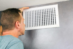 image of a man touching air vents due to an air conditioner that is blowing warm air