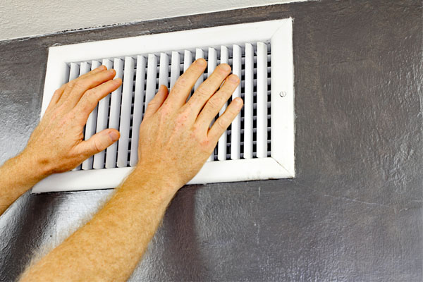 image of a homeowner placing hands in front of hvac air vent to check for airflow