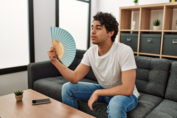 man using hand fan indoors while feeling warm due to poor HVAC airflow