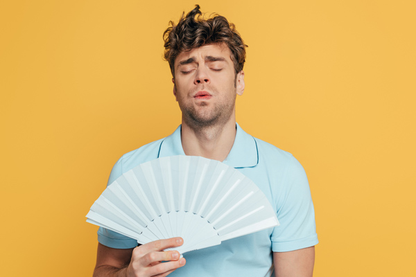 man cooling himself with a fan due to no air conditioner in room