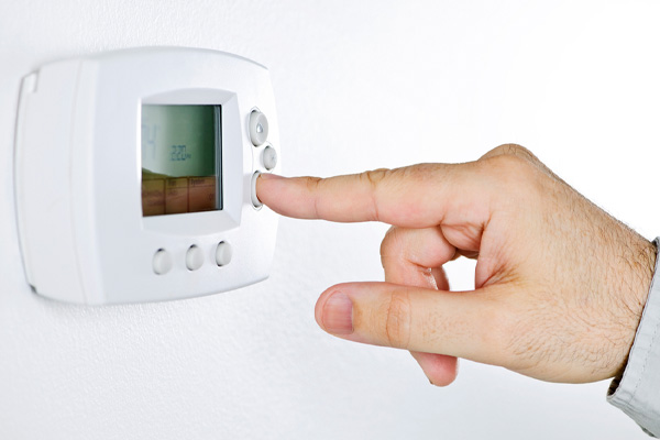 image of a homeowner adjusting thermostat for heat pump depicting auxillary and emergency heating