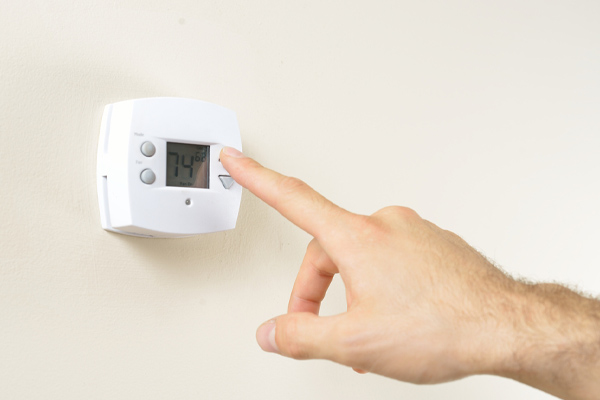image of hand adjusting thermostat due to air conditioner starting cold and then blowing warm air