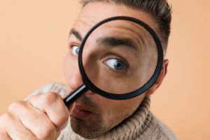 close up of a man looking through a magnifying glass depicting top signs of poor indoor air quality