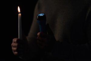 cropped image of a man holding candle and flashlight depicting power interruption