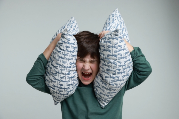 boy covering his ears with throw pillows due to furnace noise