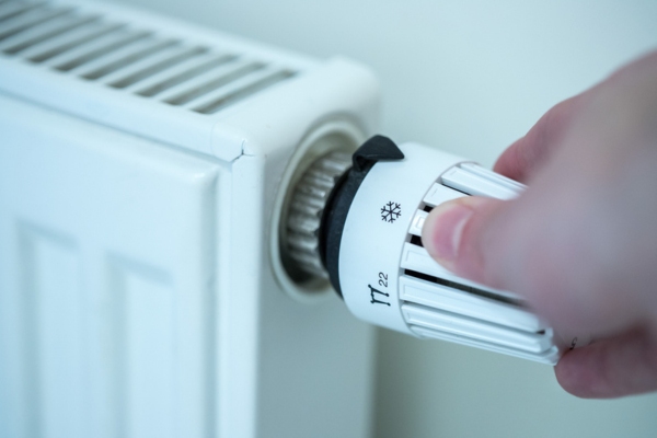 close up image of a homeowner adjusting oil heat radiator thermostat