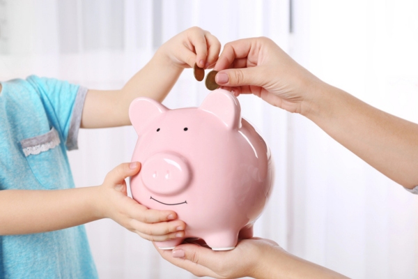 hands of kid and adult putting coin in a piggy bank depicting Financial Advantages