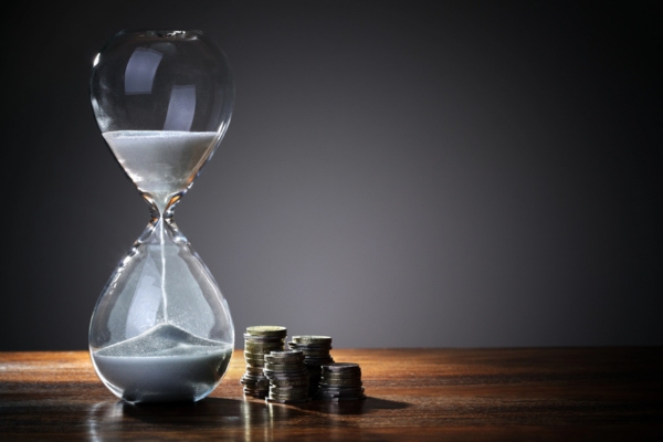 sand hourglass beside stacks of coins depicting saving time and money