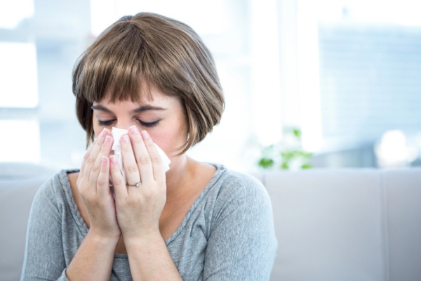 Woman sitting on a couch about to sneeze depicting Factors That Affect Air Filter Replacement Timing
