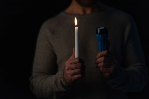 cropped view of a man holding a lit candle and a flashlight due to power outage