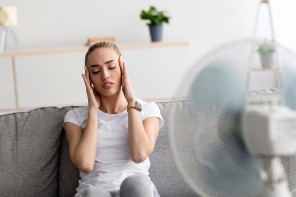 woman feeling hot indoors in front of fan due to cooling system emergency