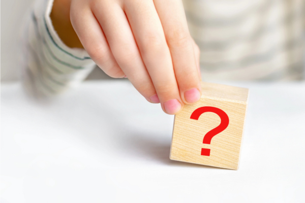 child's hand holding a question mark cube depicting Smart Thermostat vs Programmable Thermostat FAQ