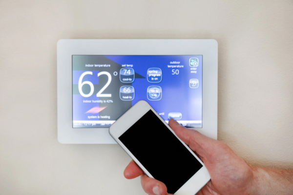 male hand holding smart phone in front of smart thermostat